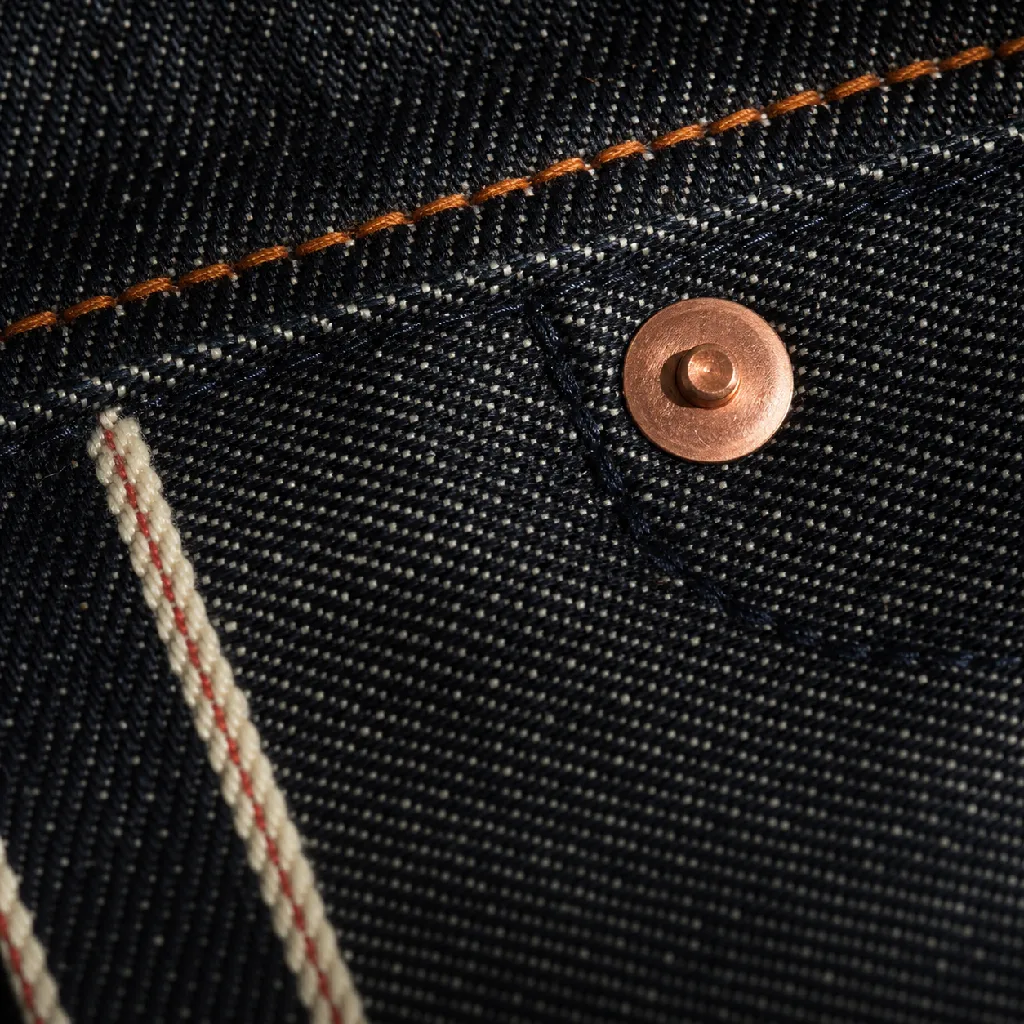 Macro of stonewash indigo selvedge denim with copper rivet and orange topstitching